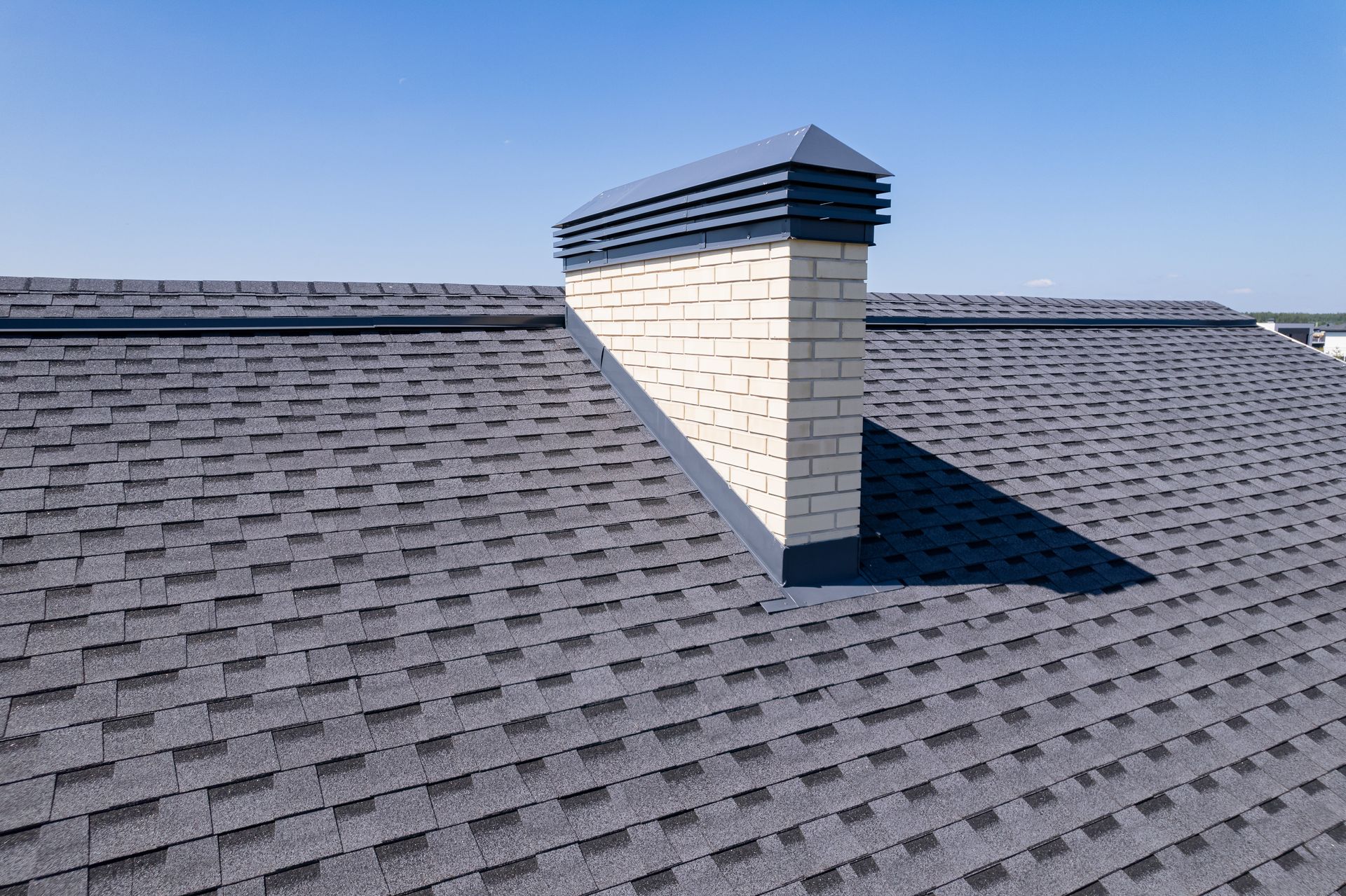 Gray shingle roof with a white chimney against a blue sky