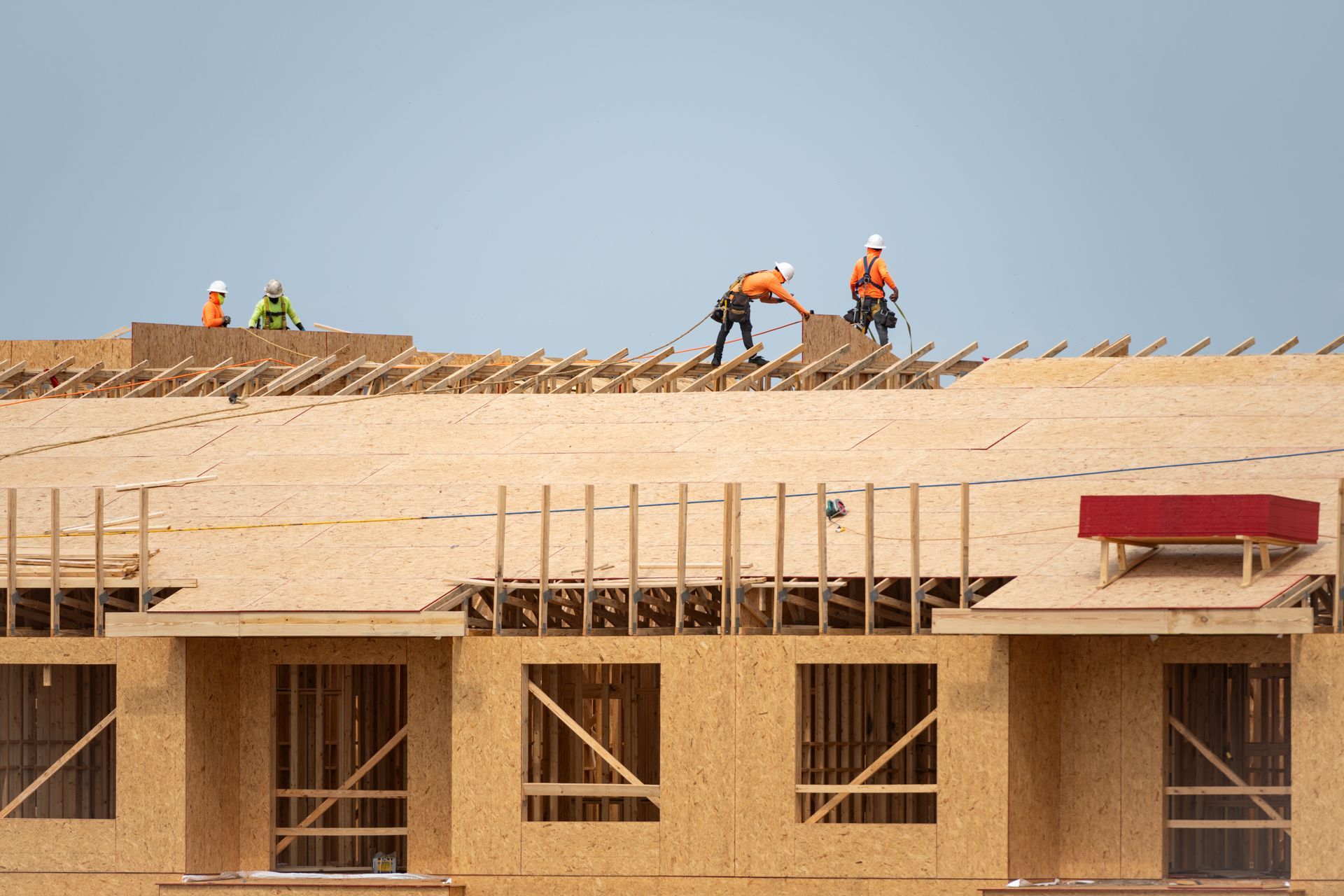 Workers roofing a building under construction, with plywood walls and a clear sky.