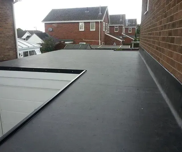 Flat rooftop walkway beside brick walls, overlooking neighboring houses on a cloudy day