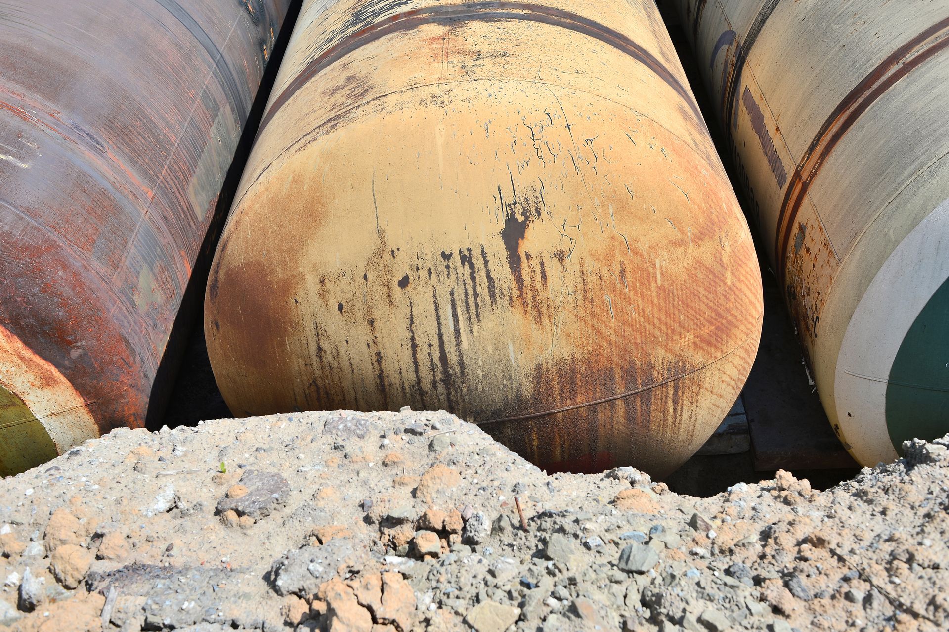 Large rusted metal pipes stacked on gravel, viewed close up.