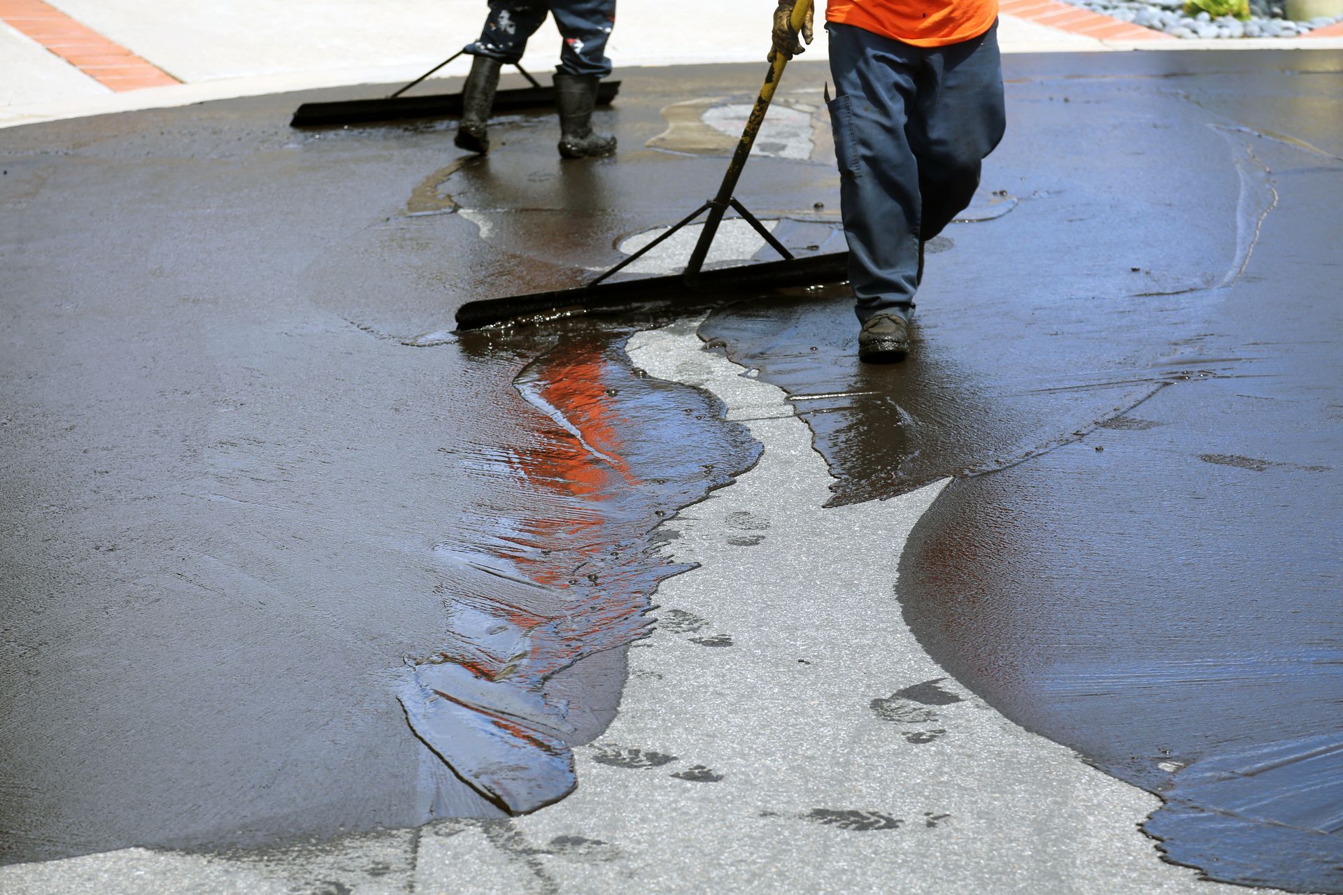 Workers squeegeeing water off a wet street, reflecting orange and gray colors on the pavement