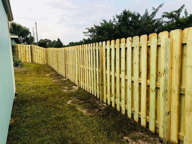 Wooden picket fence along a grassy backyard, connecting to a light blue house.