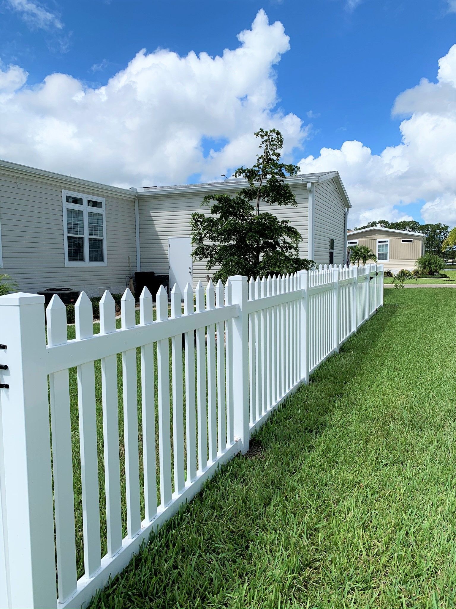 White picket fence in front of a light-colored building with a blue sky and clouds overhead.