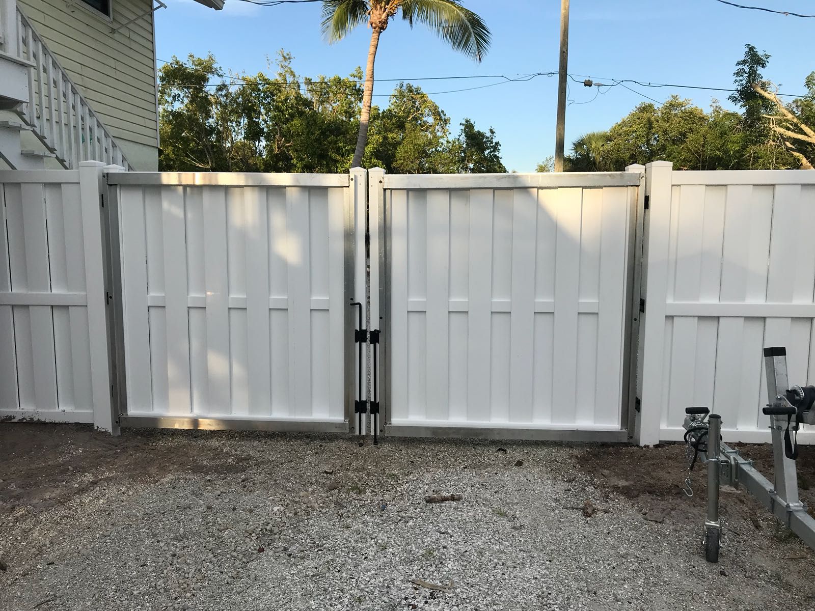 White gate in a gravel driveway, part of a white vinyl fence.