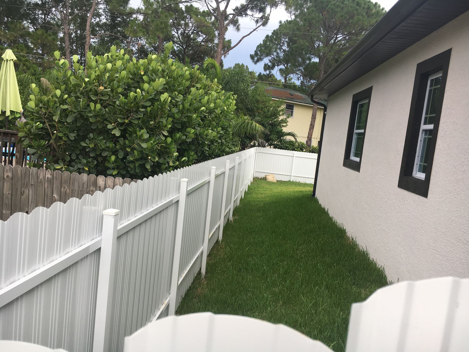 White fence along a grassy backyard, adjacent to a beige house with dark window frames.