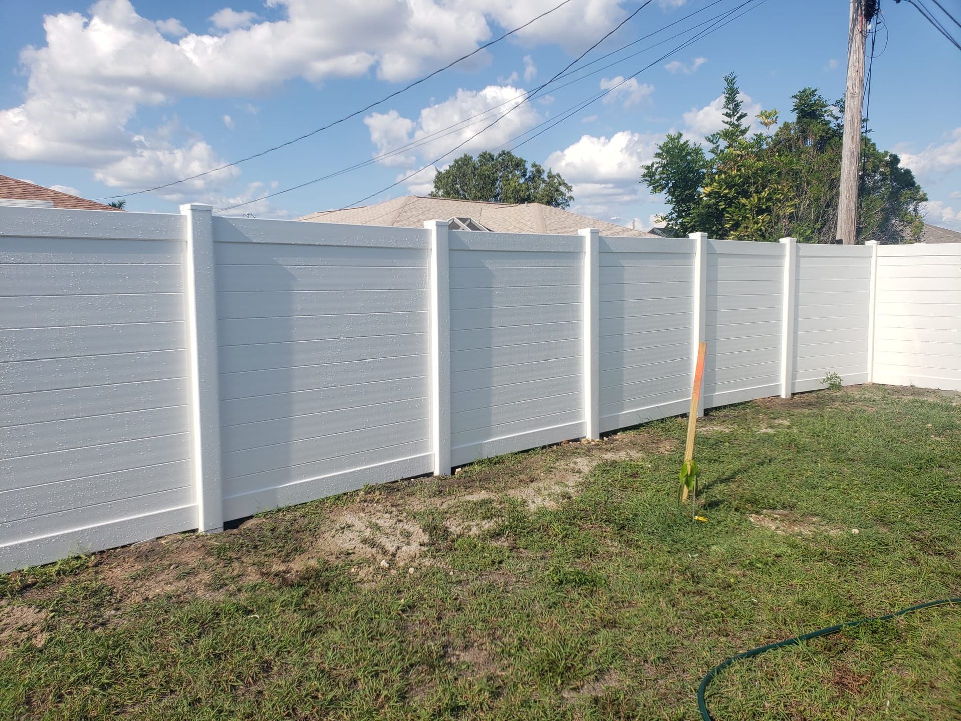 White vinyl privacy fence in a grassy yard under a blue sky with some clouds.