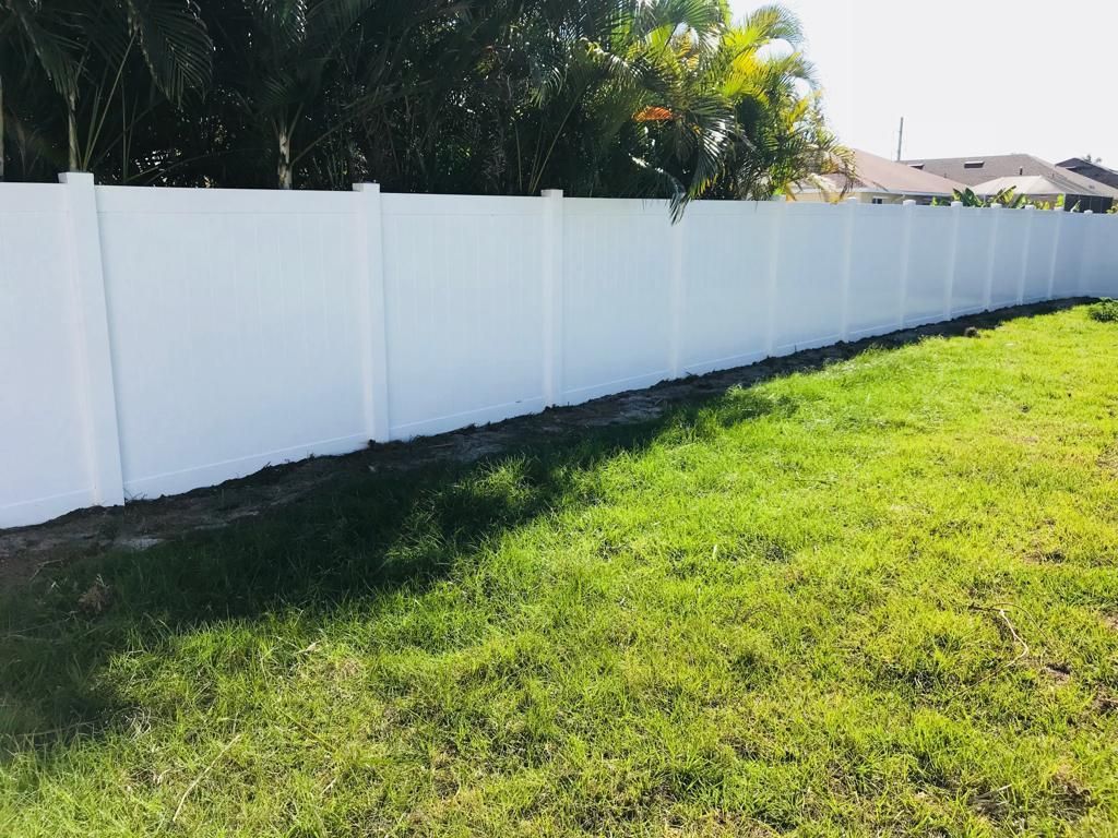 White vinyl fence bordering a grassy yard with trees and houses in the background.