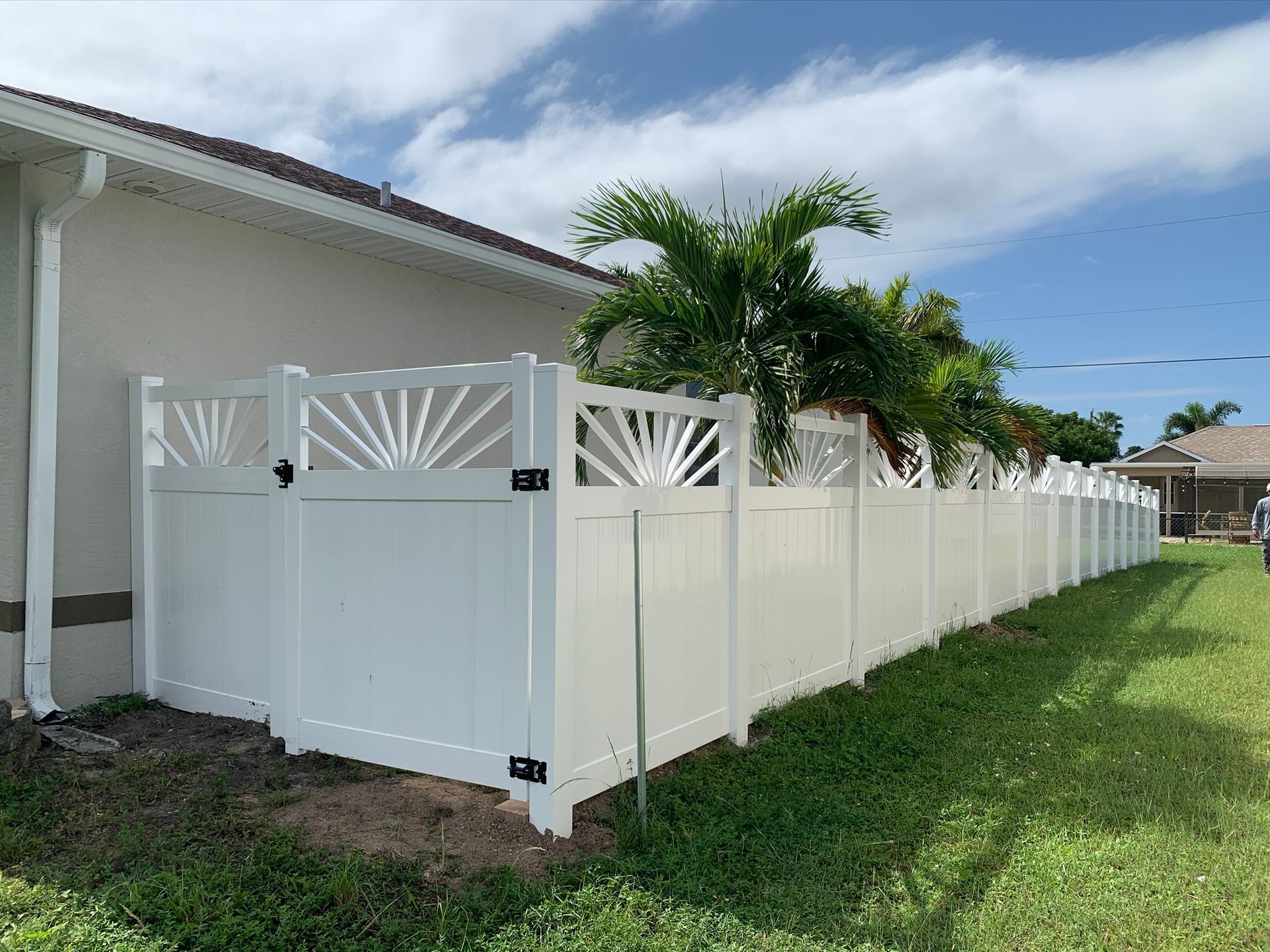 White vinyl fence with decorative sunburst tops along a grassy yard, beside a beige house.
