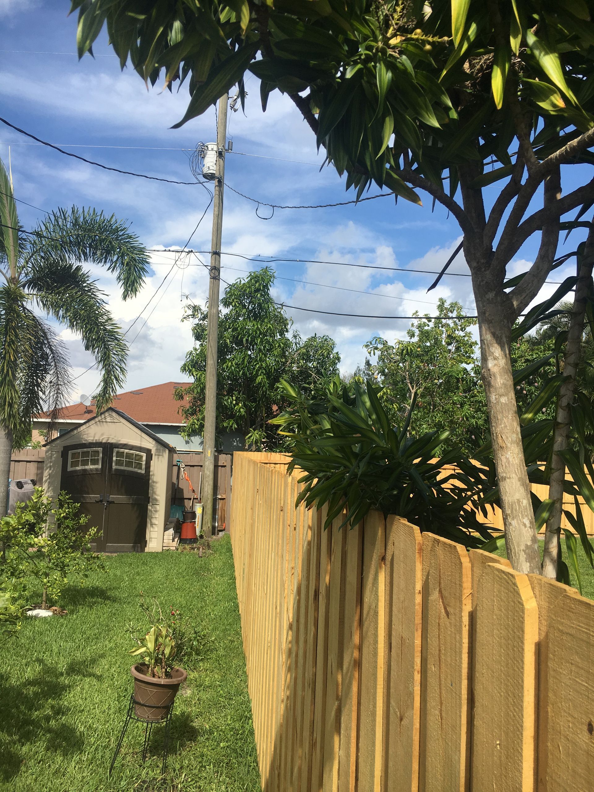 Wooden fence in a backyard with a garage, trees, power lines, and a blue sky.