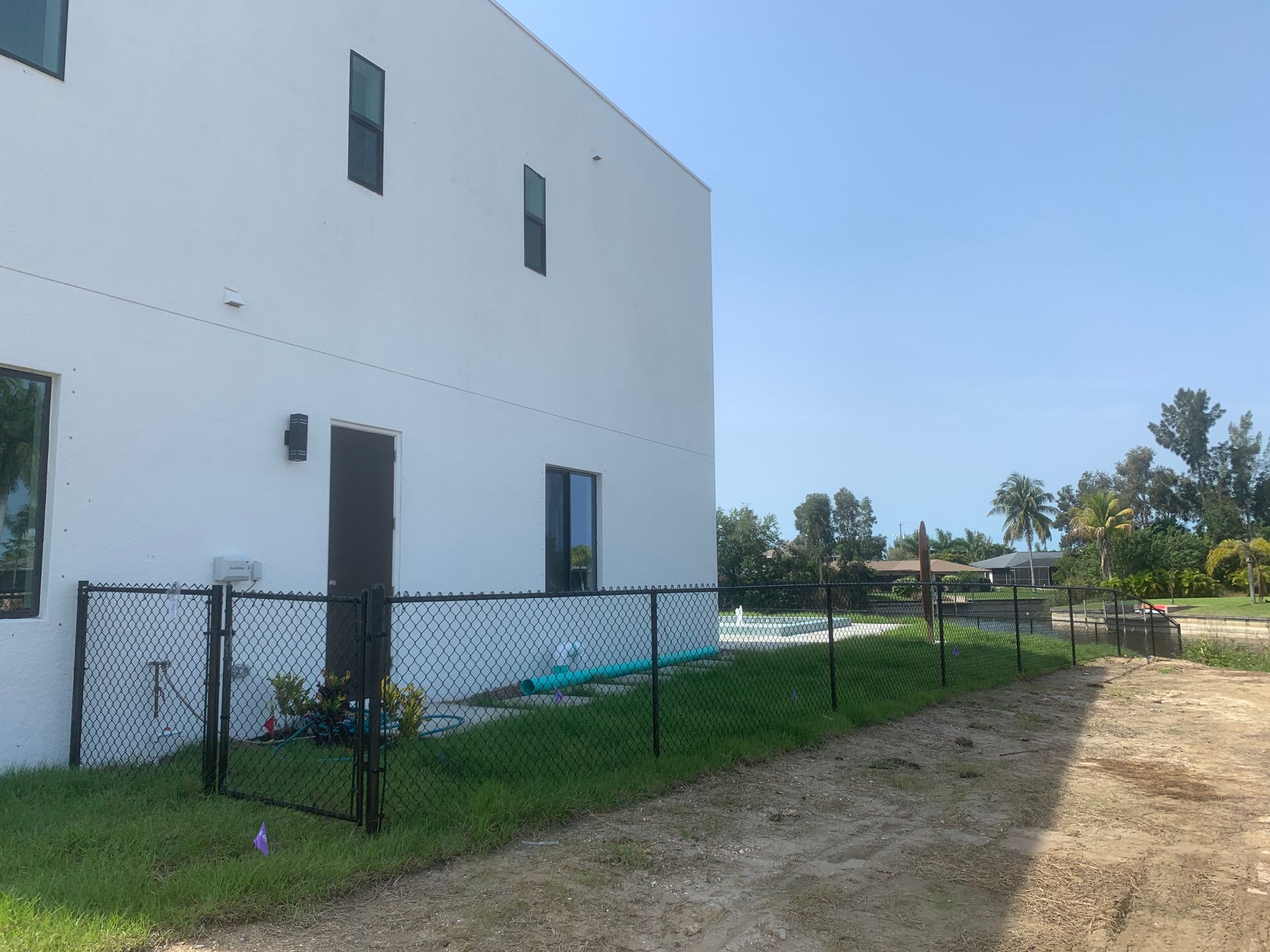 White building with black fence, green grass, and dirt path on a sunny day.