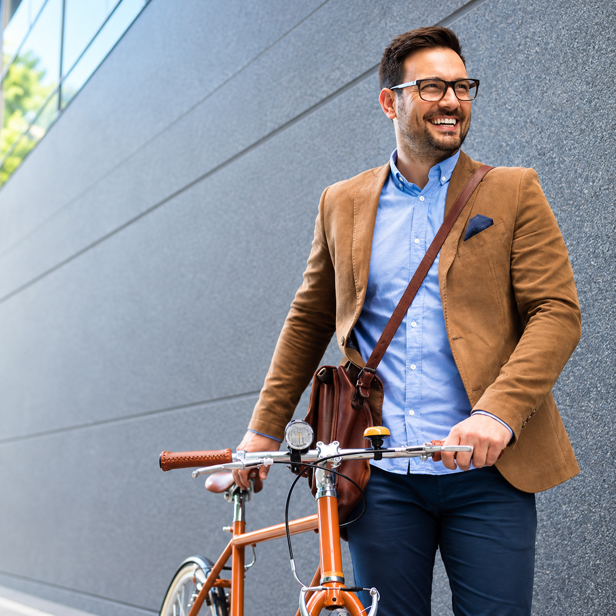 Man smiling beside an orange bicycle, wearing a tan blazer on a city sidewalk.