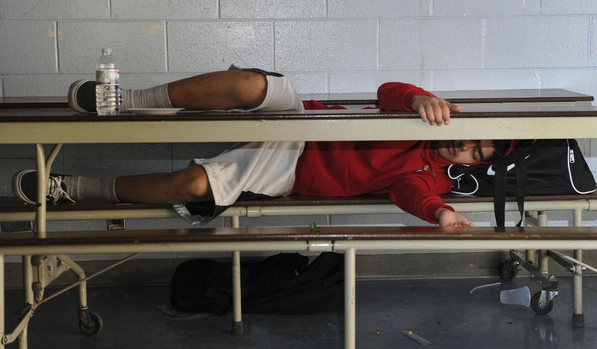 A person in a red hoodie is laying under a table