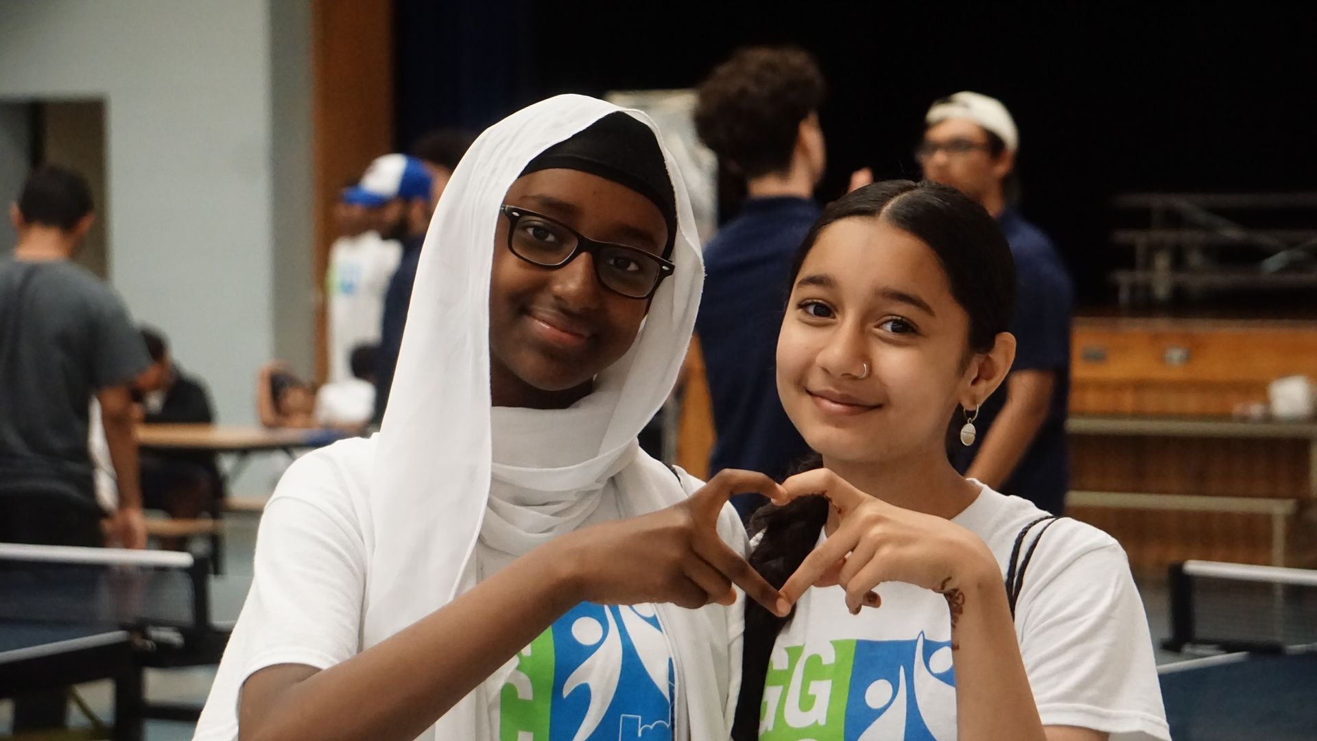 Two young girls are making a heart shape with their hands.