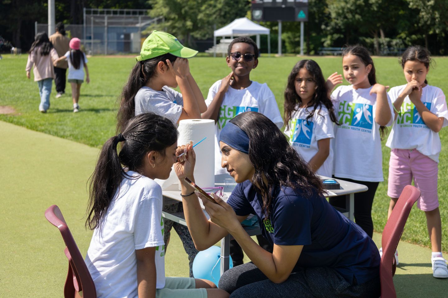 A woman is painting a girl 's face in a park.