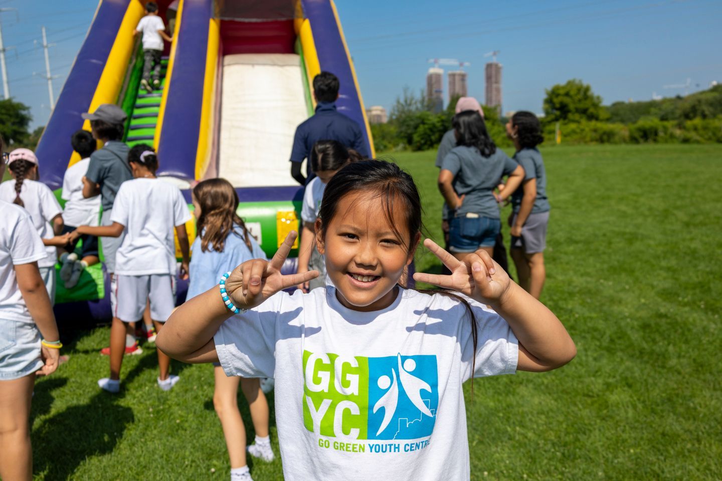 A young girl is making a peace sign in front of an inflatable slide.