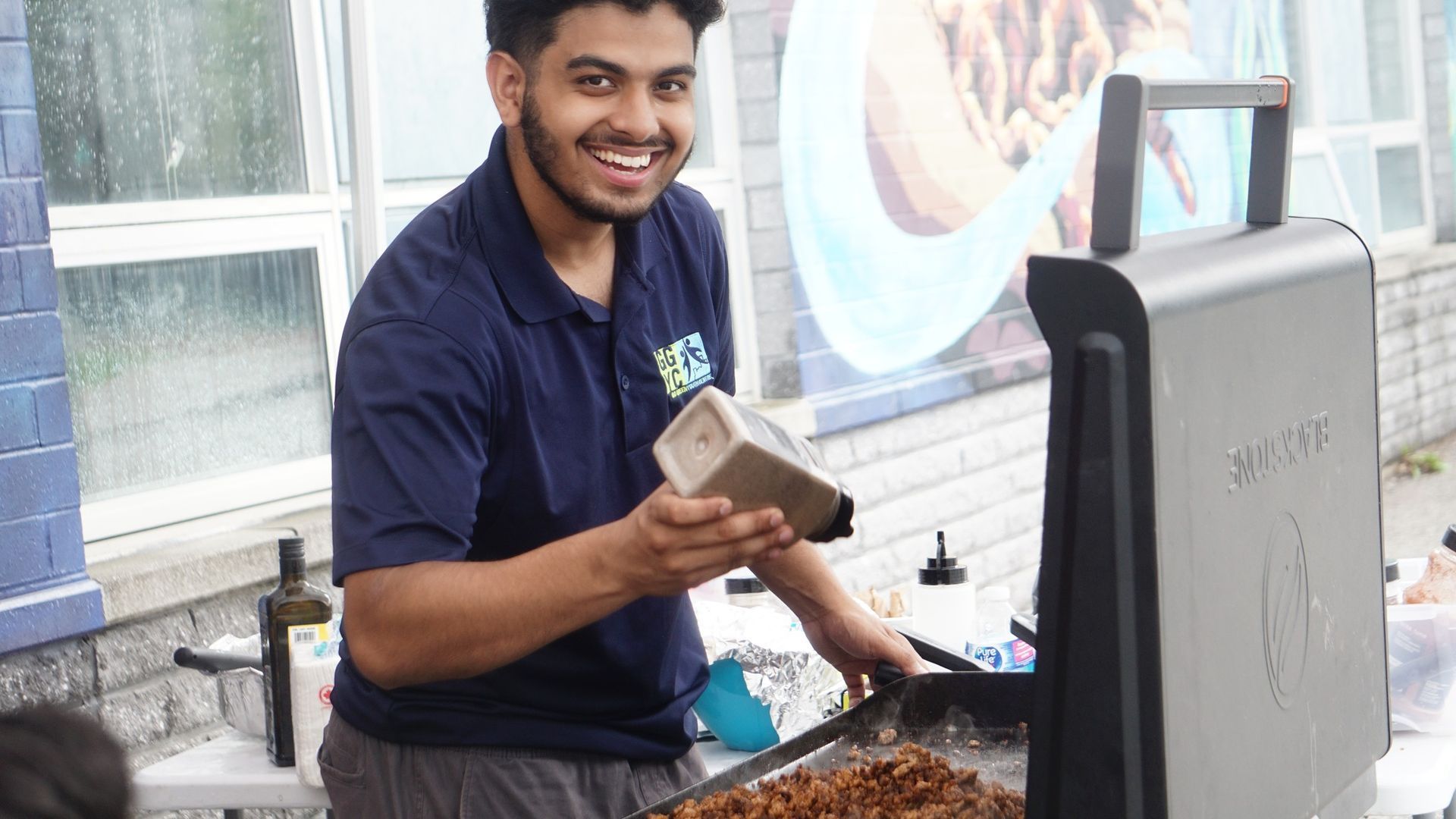 A man is standing in front of a grill cooking food.