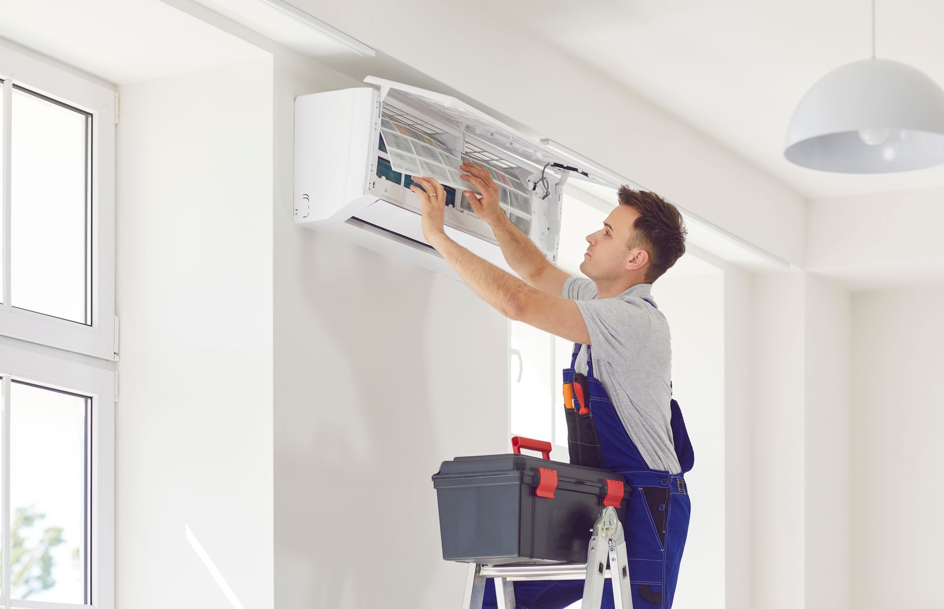 Technician cleaning a wall-mounted air conditioner in a bright room
