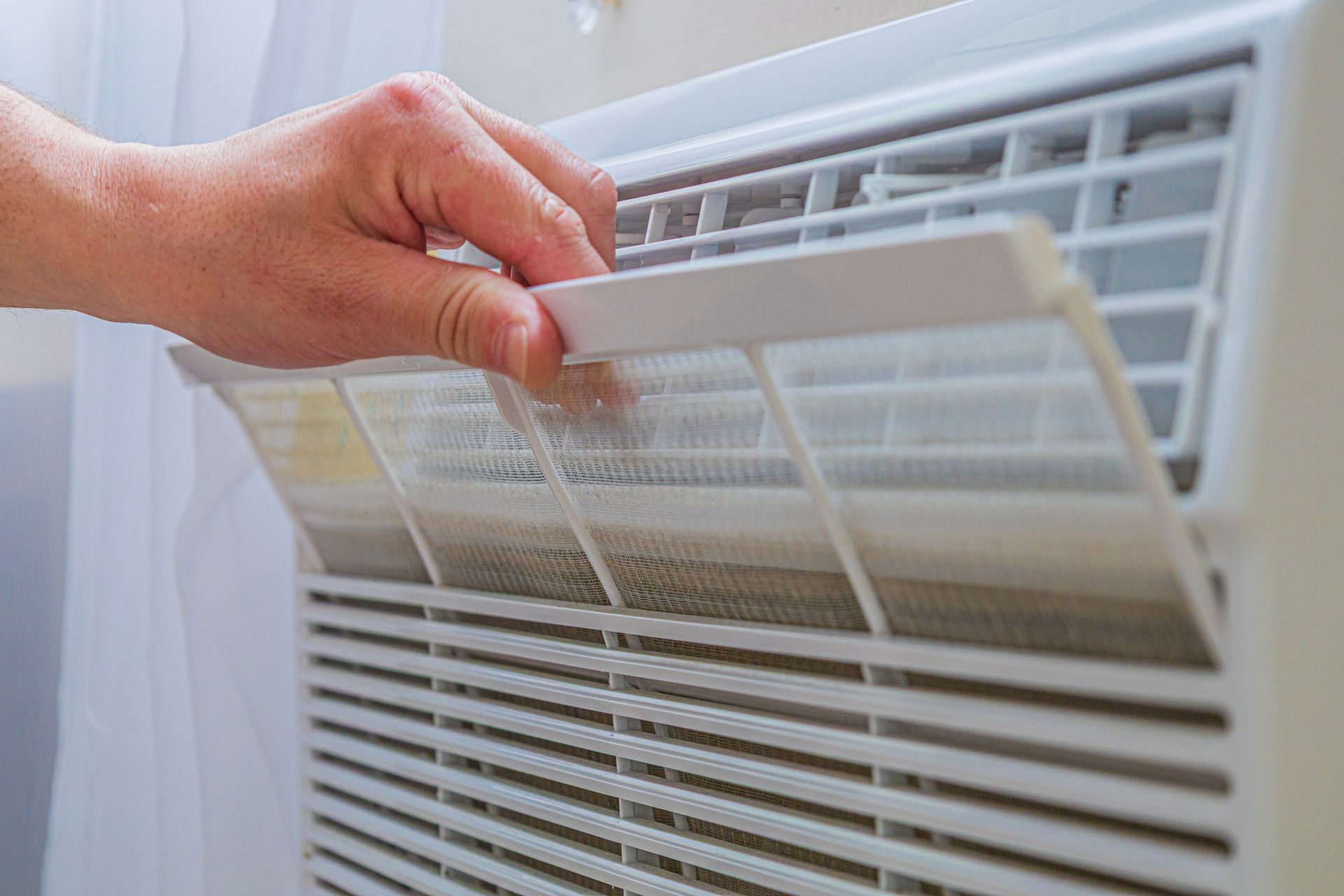 Hand removing a dirty air conditioner filter from a white window unit