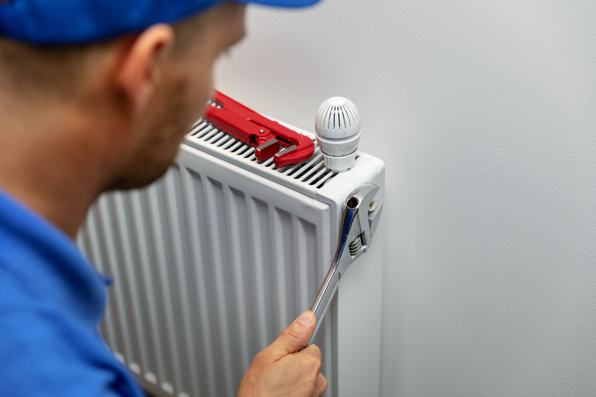 Person using a wrench to adjust a white radiator with a red wrench on top
