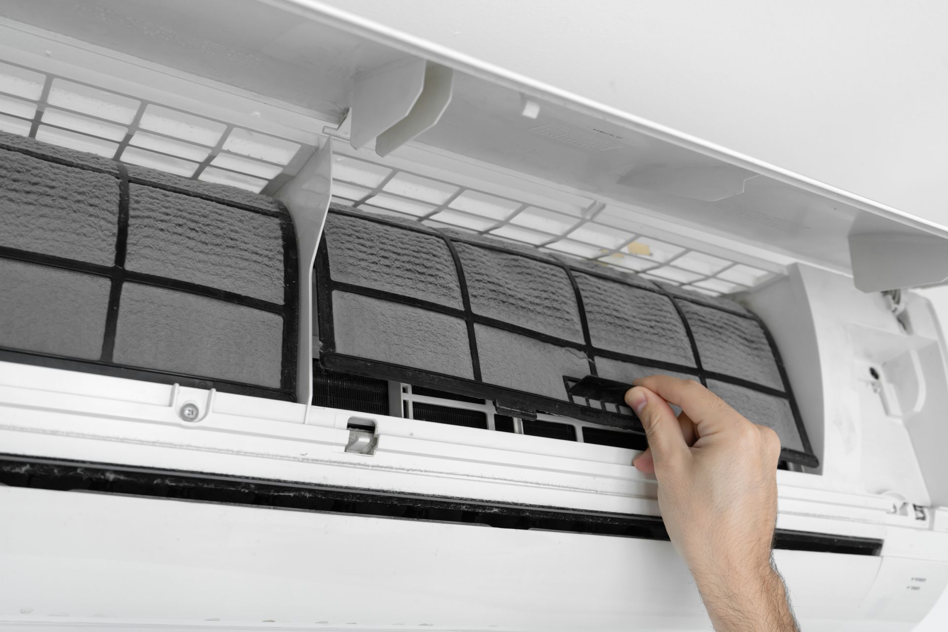 Hand opening a wall-mounted air conditioner filter for cleaning