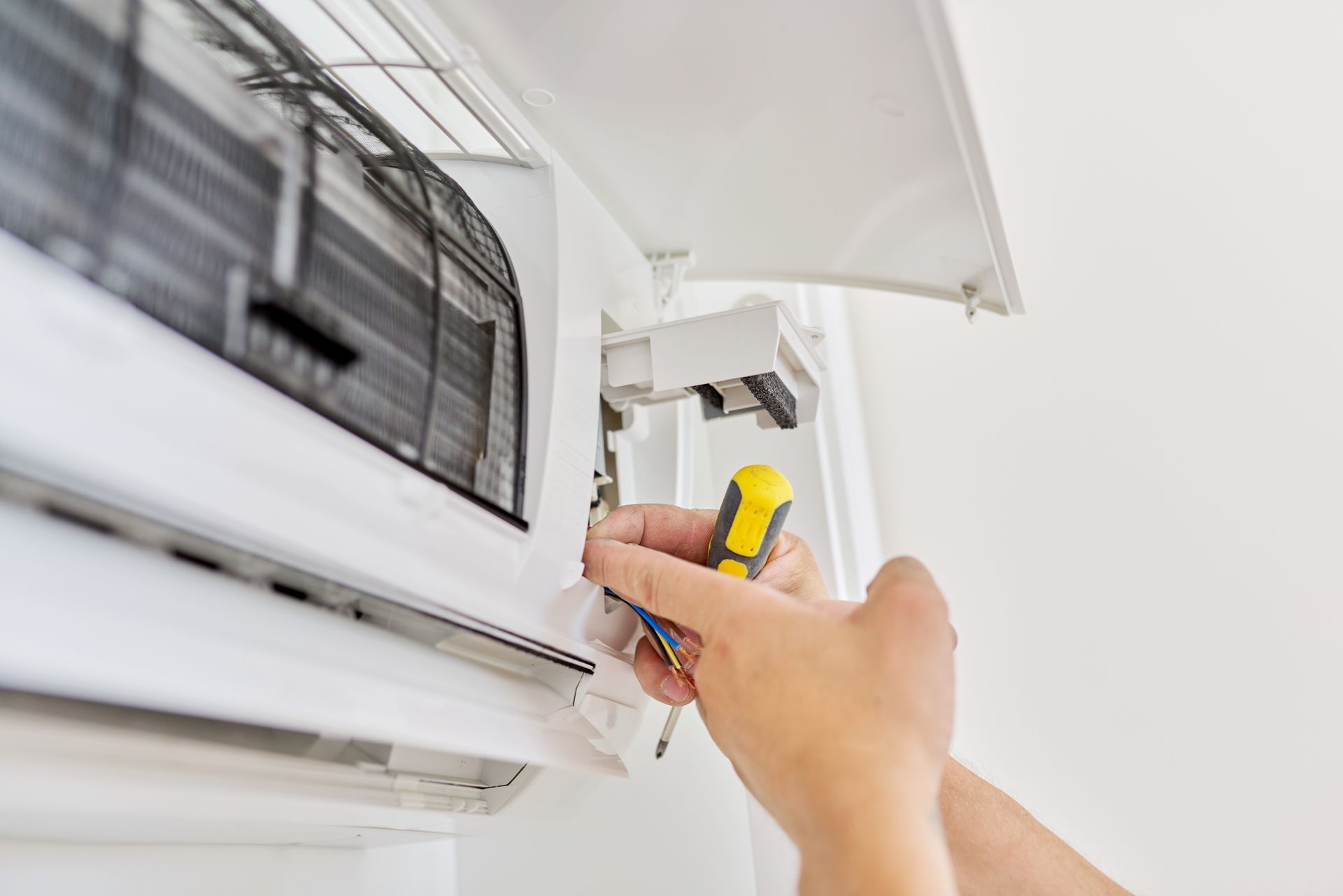 Hand adjusting a window air conditioner with a screwdriver beside a white wall.