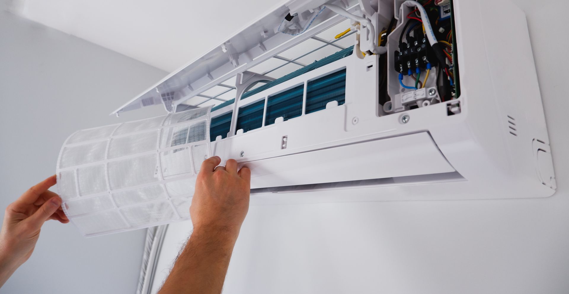 Hands removing the filter from a wall-mounted air conditioner with the cover open