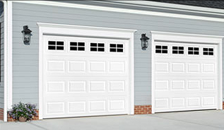 A couple of white garage doors on the side of a house.