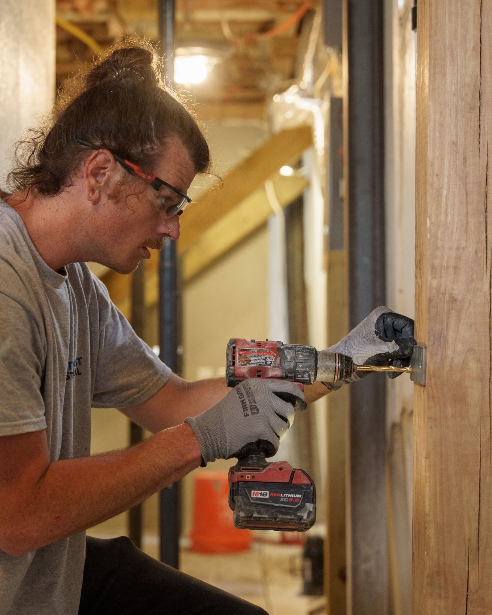 Worker using a power drill on a wooden beam in an unfinished indoor construction area