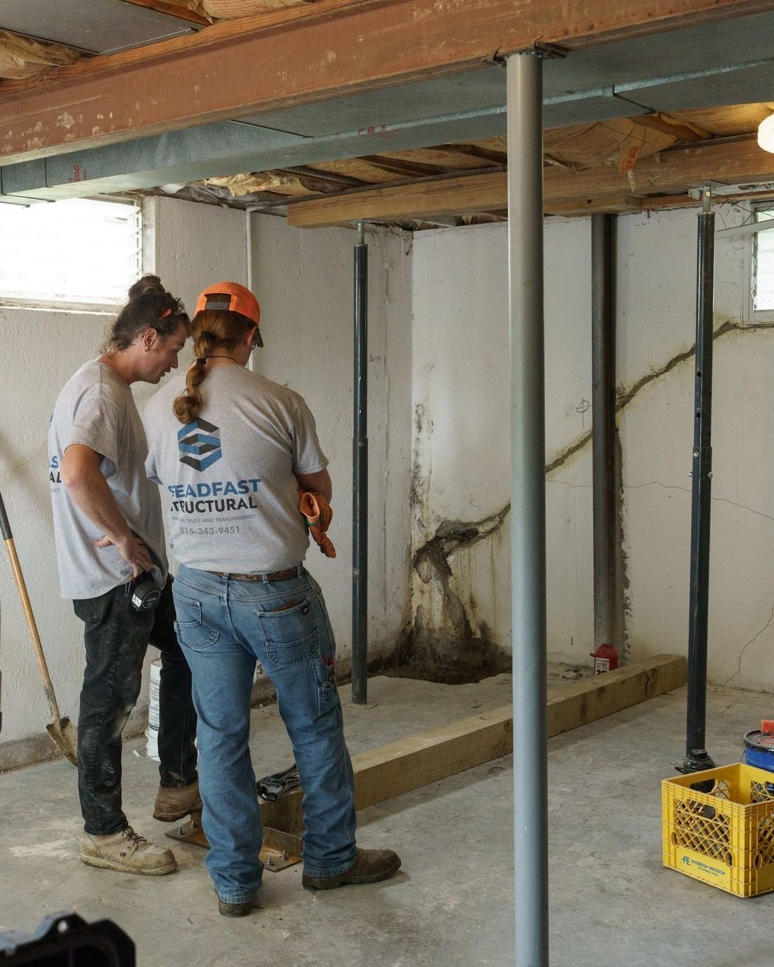 Two workers inspecting pipes and walls in a partially renovated basement.