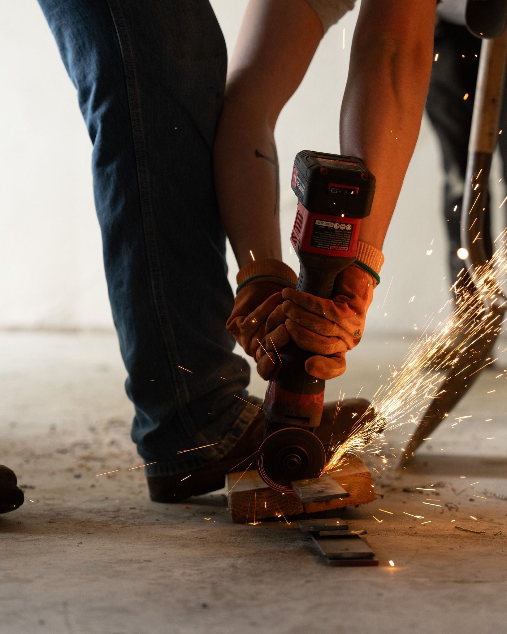 Worker using a power grinder on metal, sending sparks across a concrete floor.