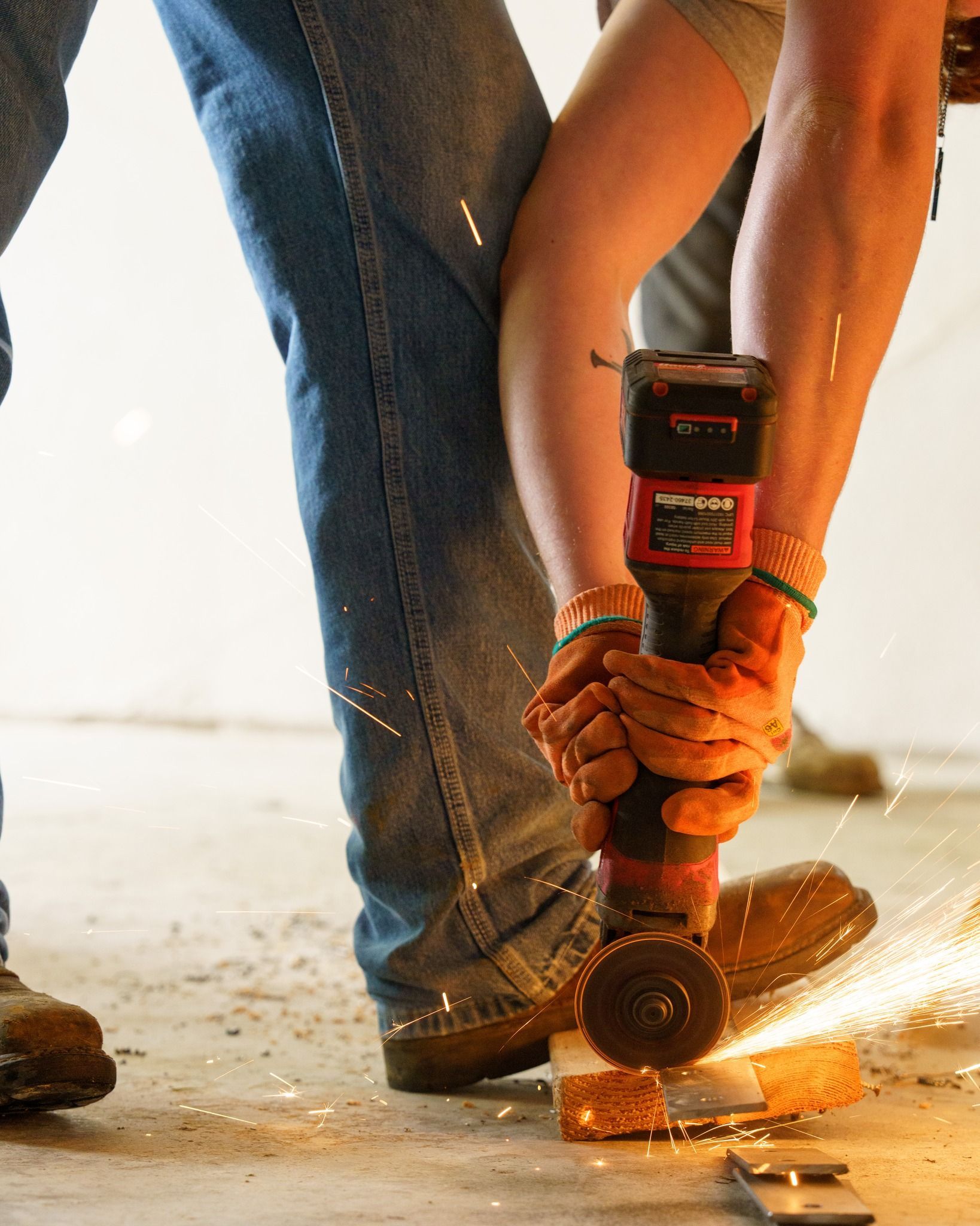 Person using a red power drill to bore into a concrete floor, with sparks flying.