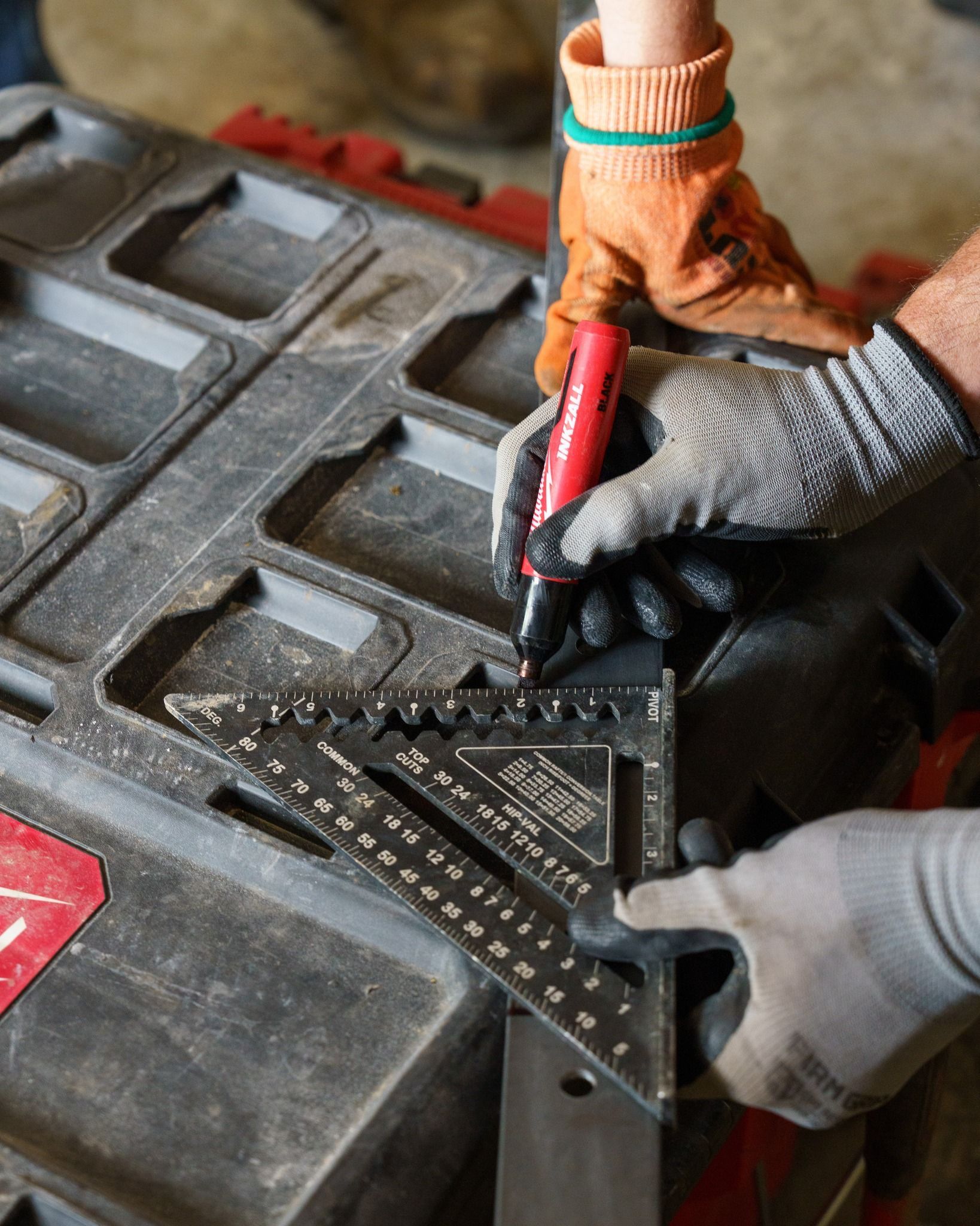 Gloved hands using red-handled cutters to trim a black metal sheet on a workbench