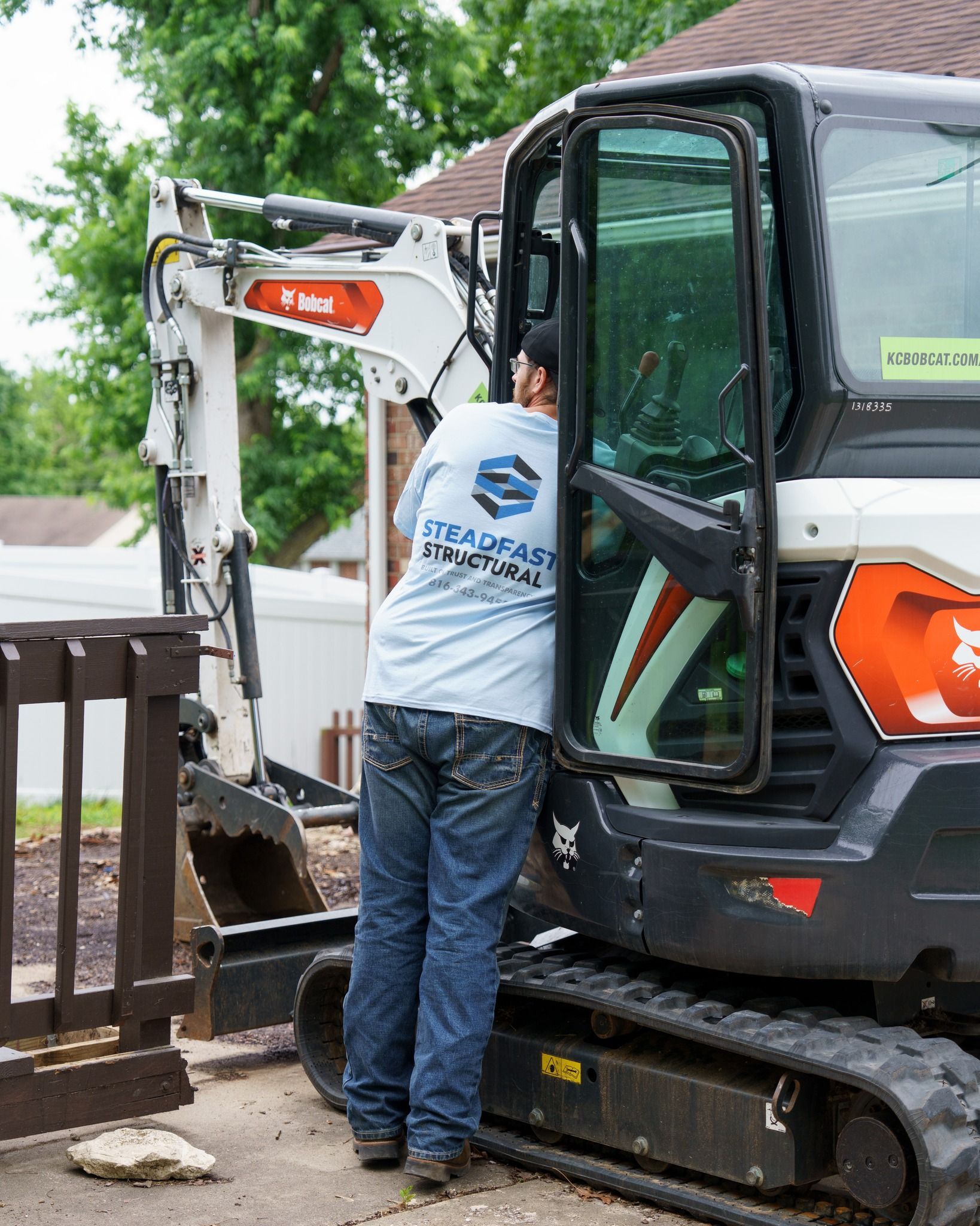 Worker operating a compact excavator beside a wooden fence at a house site