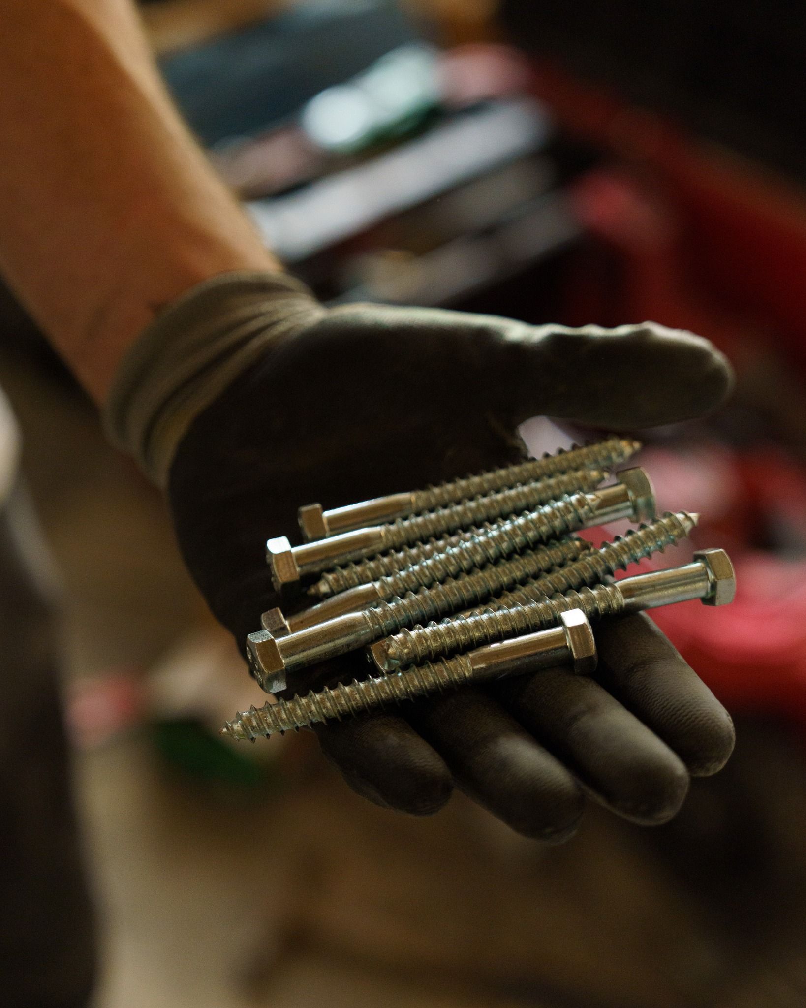 Gloved hand holding several spark plugs, with a blurred automotive background