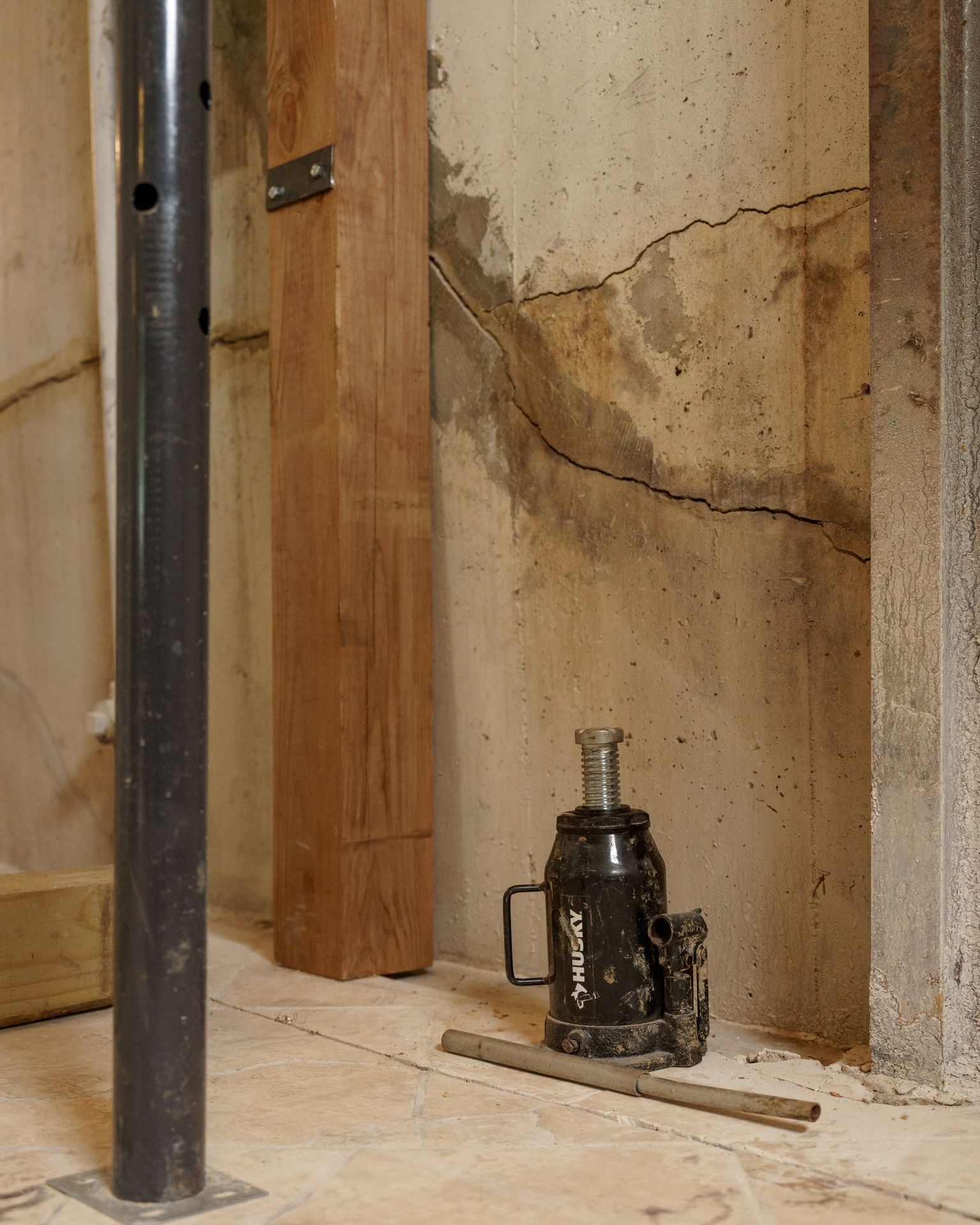 Basement wall with a large crack, a jack under a wooden beam, and a support pole in the foreground