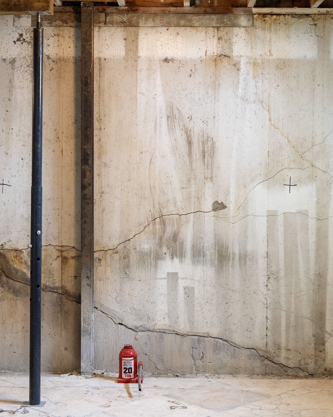 Weathered concrete wall with stains and cracks, a black pole on the left, and a red fire extinguisher below.