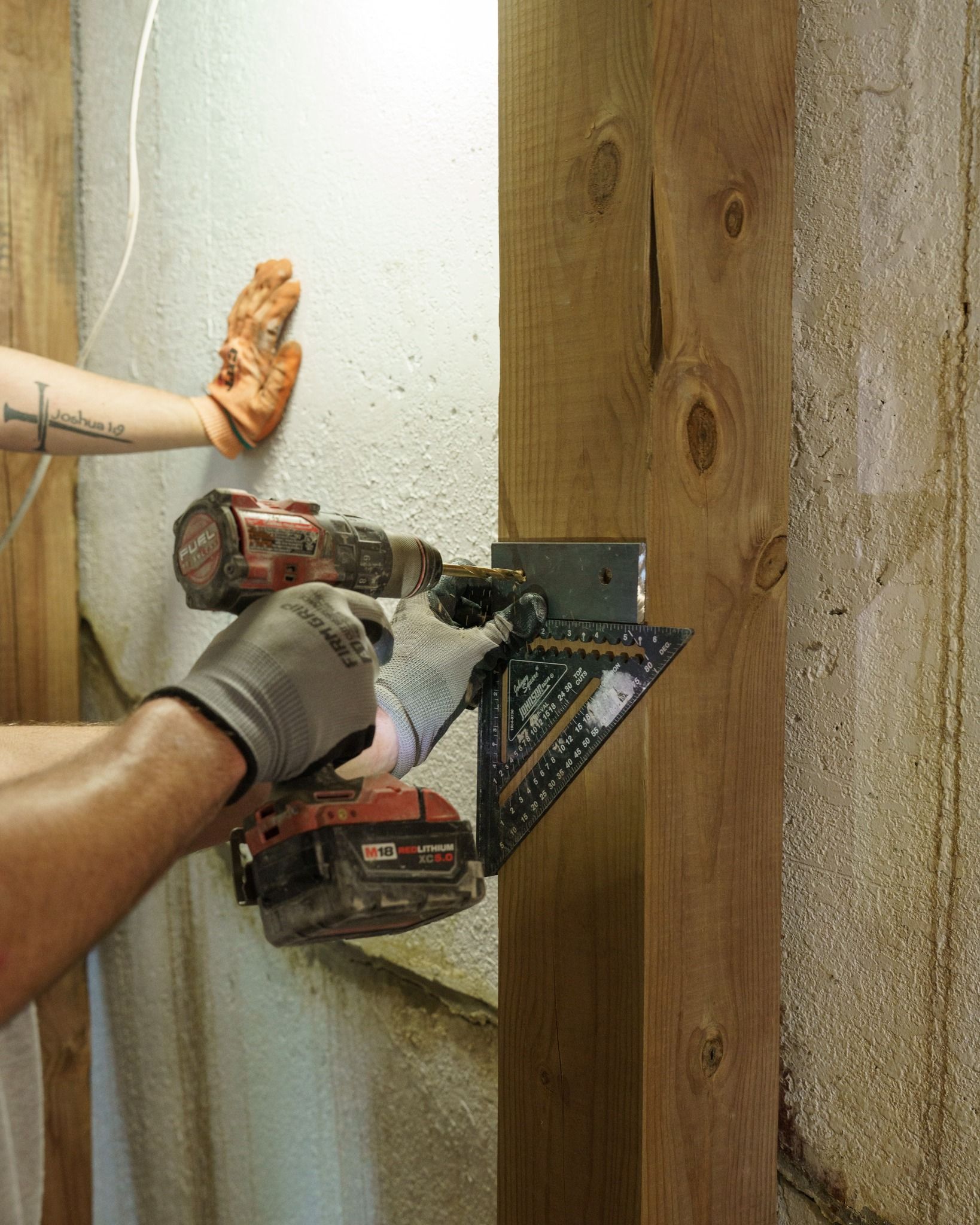 Person using a power drill to attach a metal bracket to a wooden post indoors