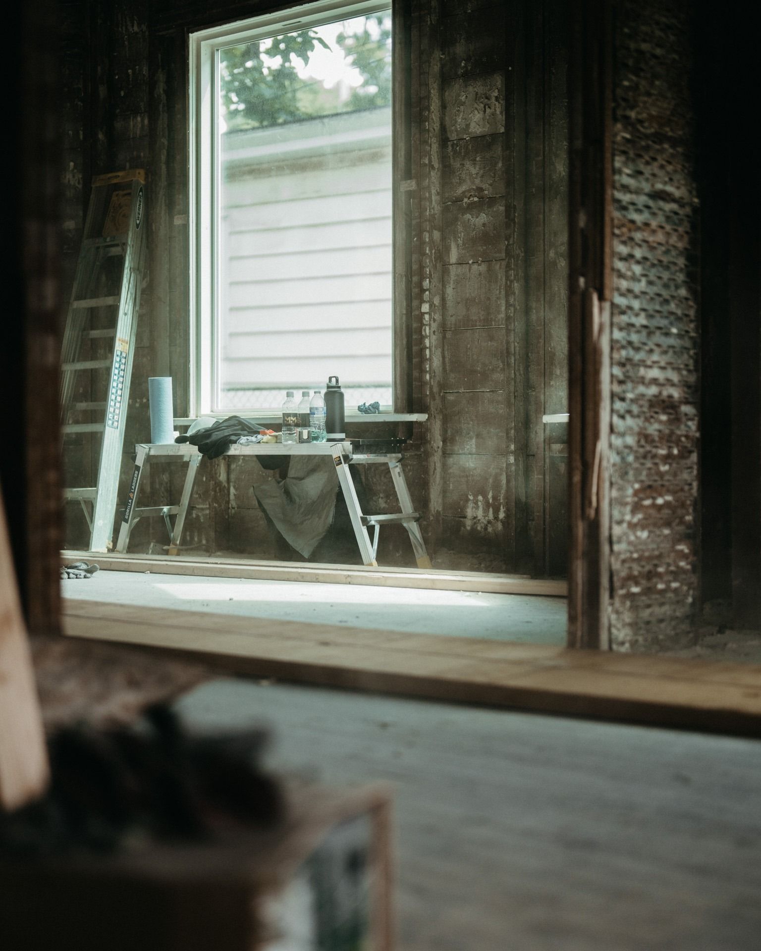 Dusty, sunlit room with a small table by a window and a mirror leaning against the wall.