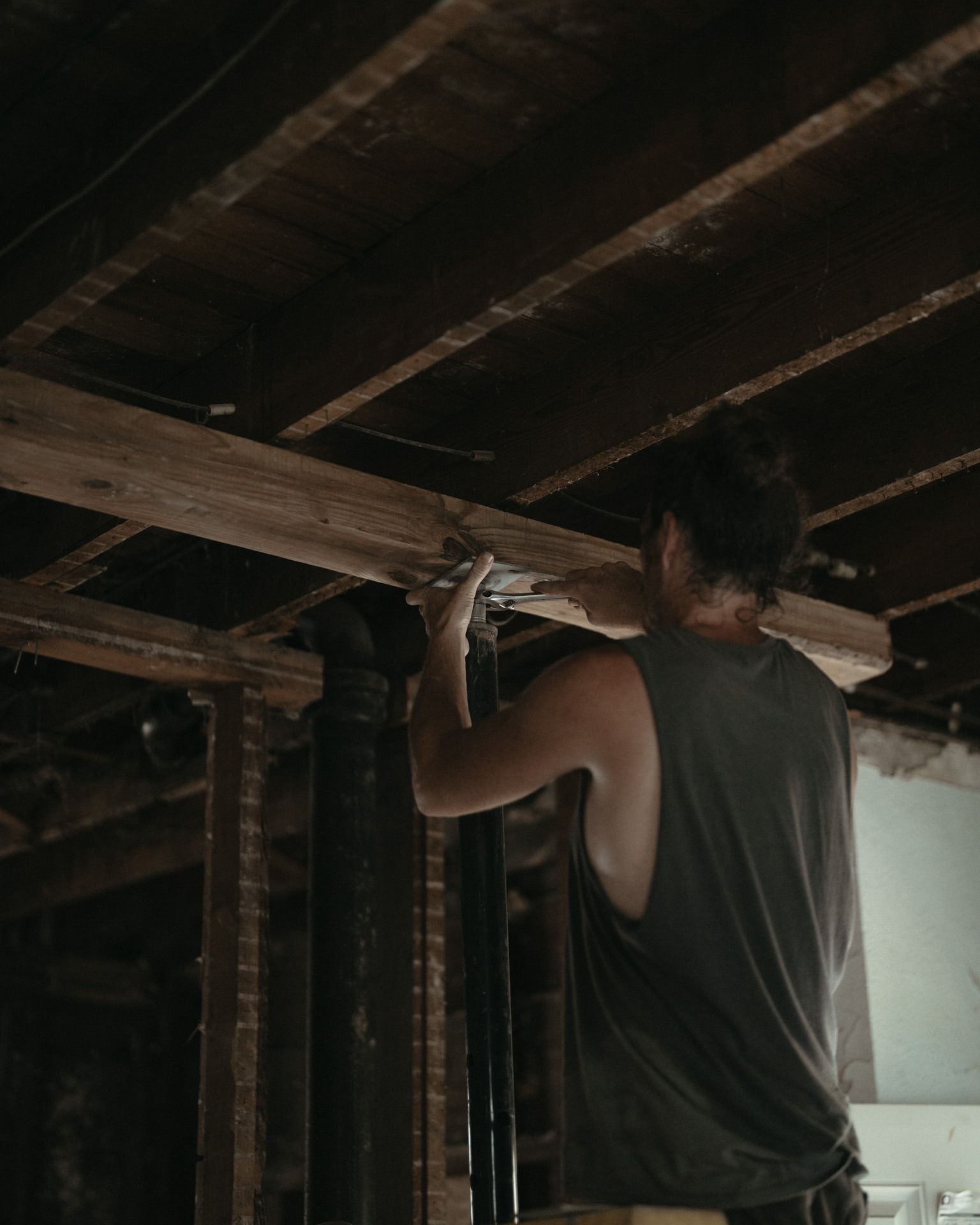 Worker installing wiring under exposed wooden ceiling beams in a dim room
