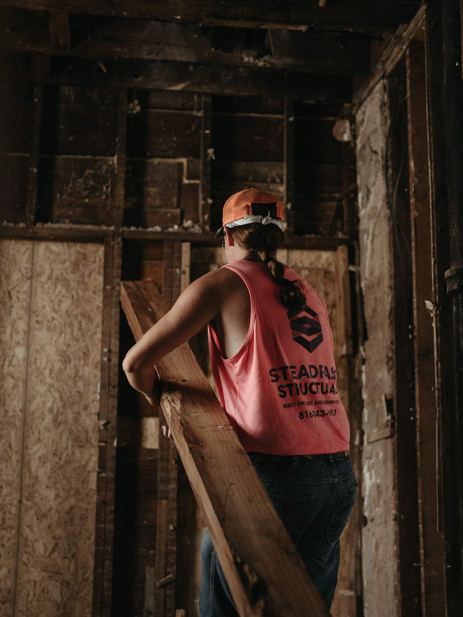 Worker in orange hard hat and red vest standing in a wooden construction frame