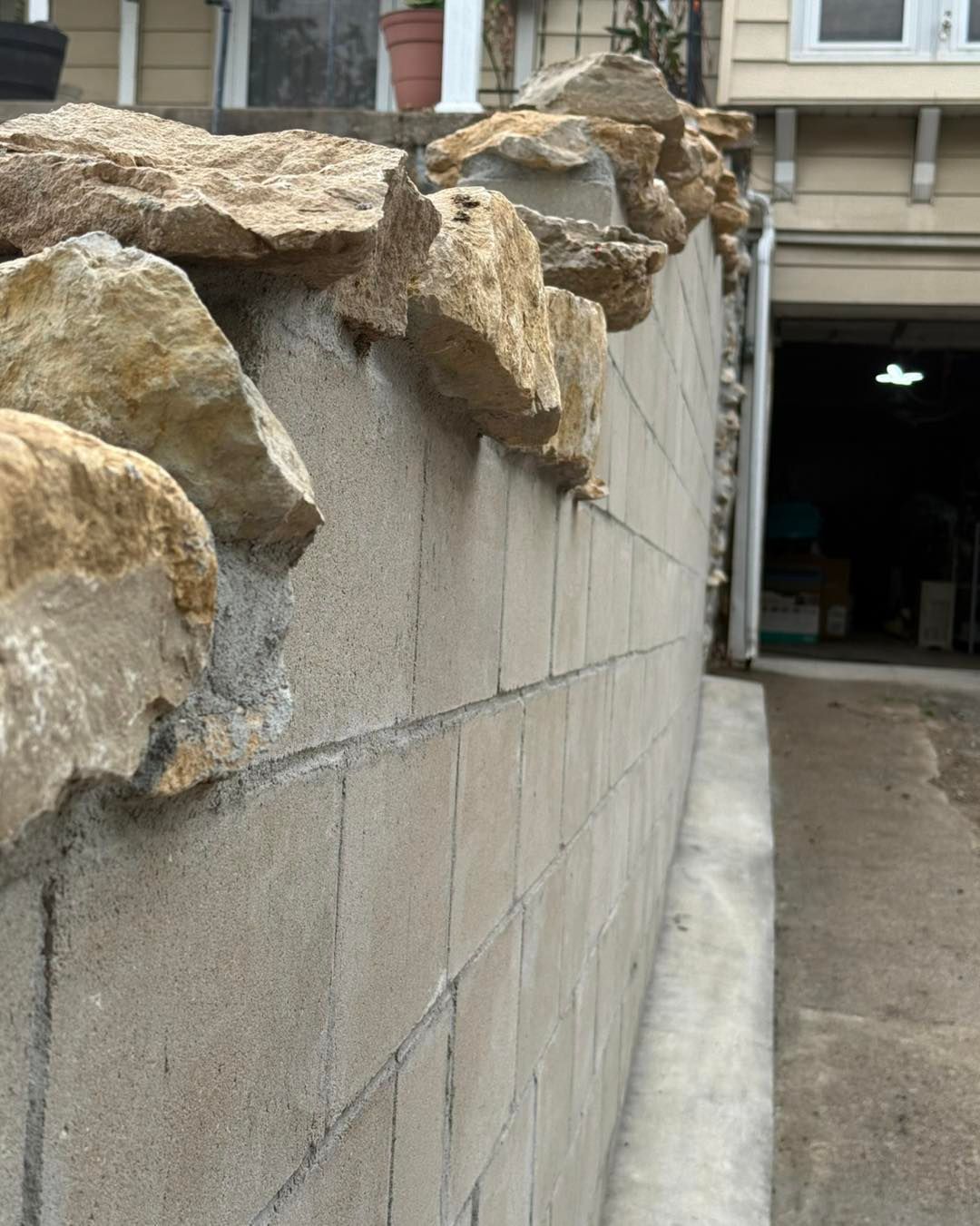 Stone retaining wall beside a driveway, topped with large rocks, leading to a garage opening.