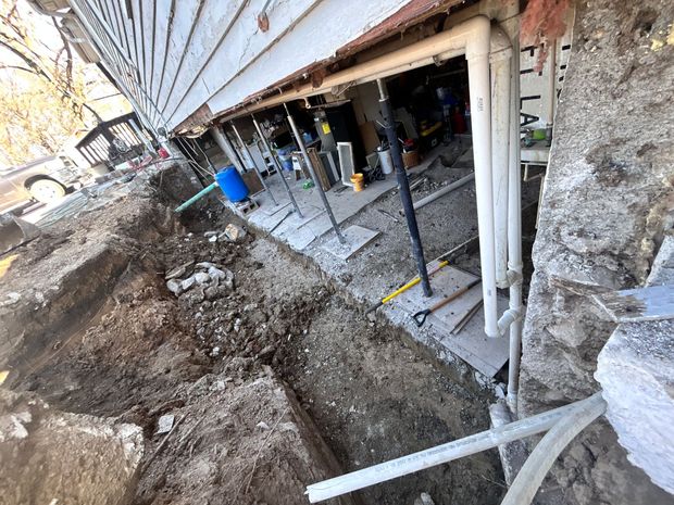 Basement excavation beside a house, with exposed foundation walls, dirt piles, and construction tools.