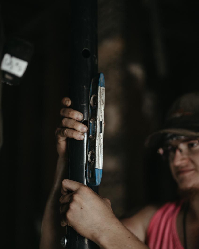 Person in a hat holding a black rifle with a blue attachment, indoors in dim light.