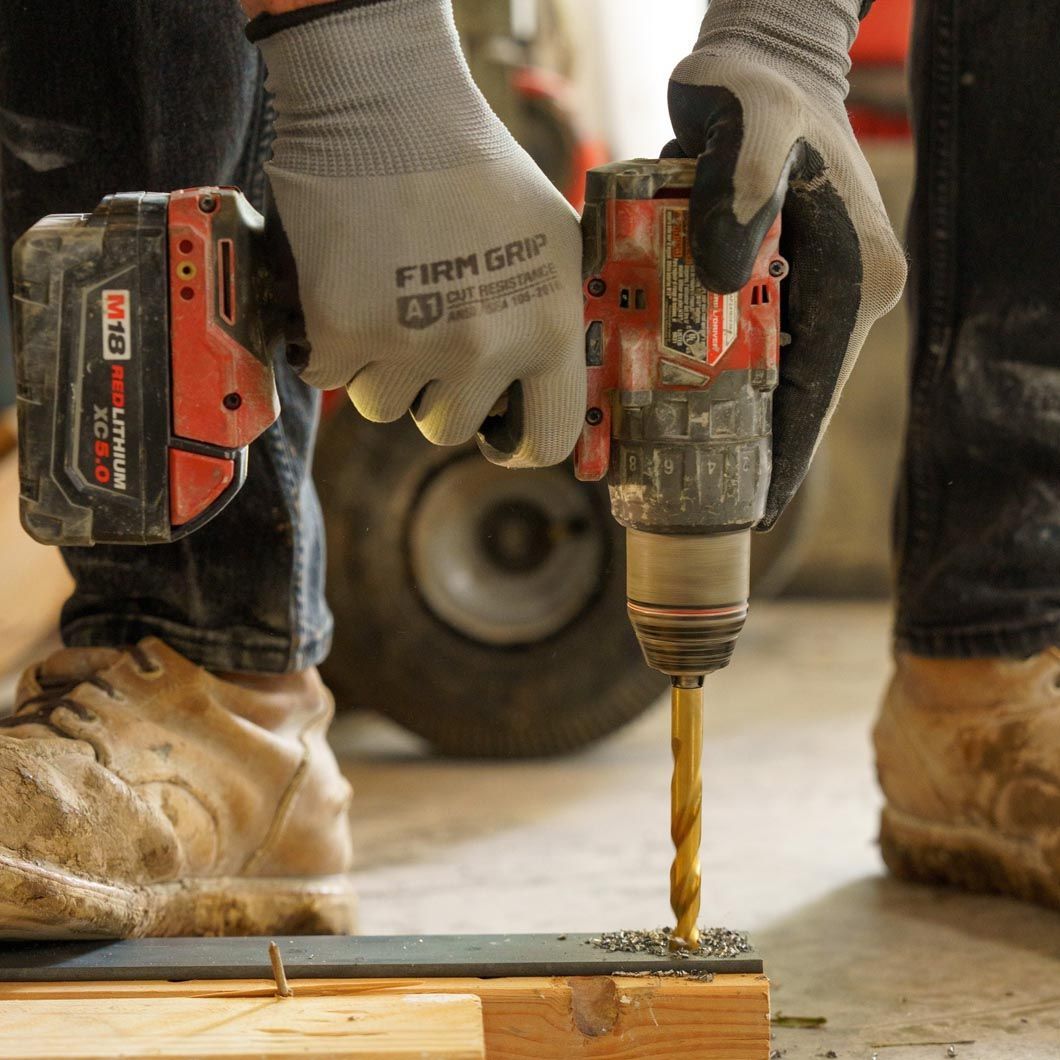 Worker drilling into wood with a power drill, wearing gloves and boots on a construction site