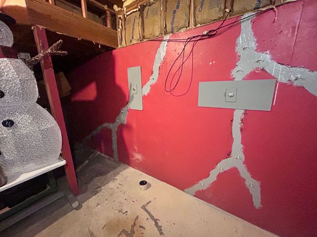 Red wall with white cracks, electrical outlets, and a cluttered shelf in a basement-like corner.