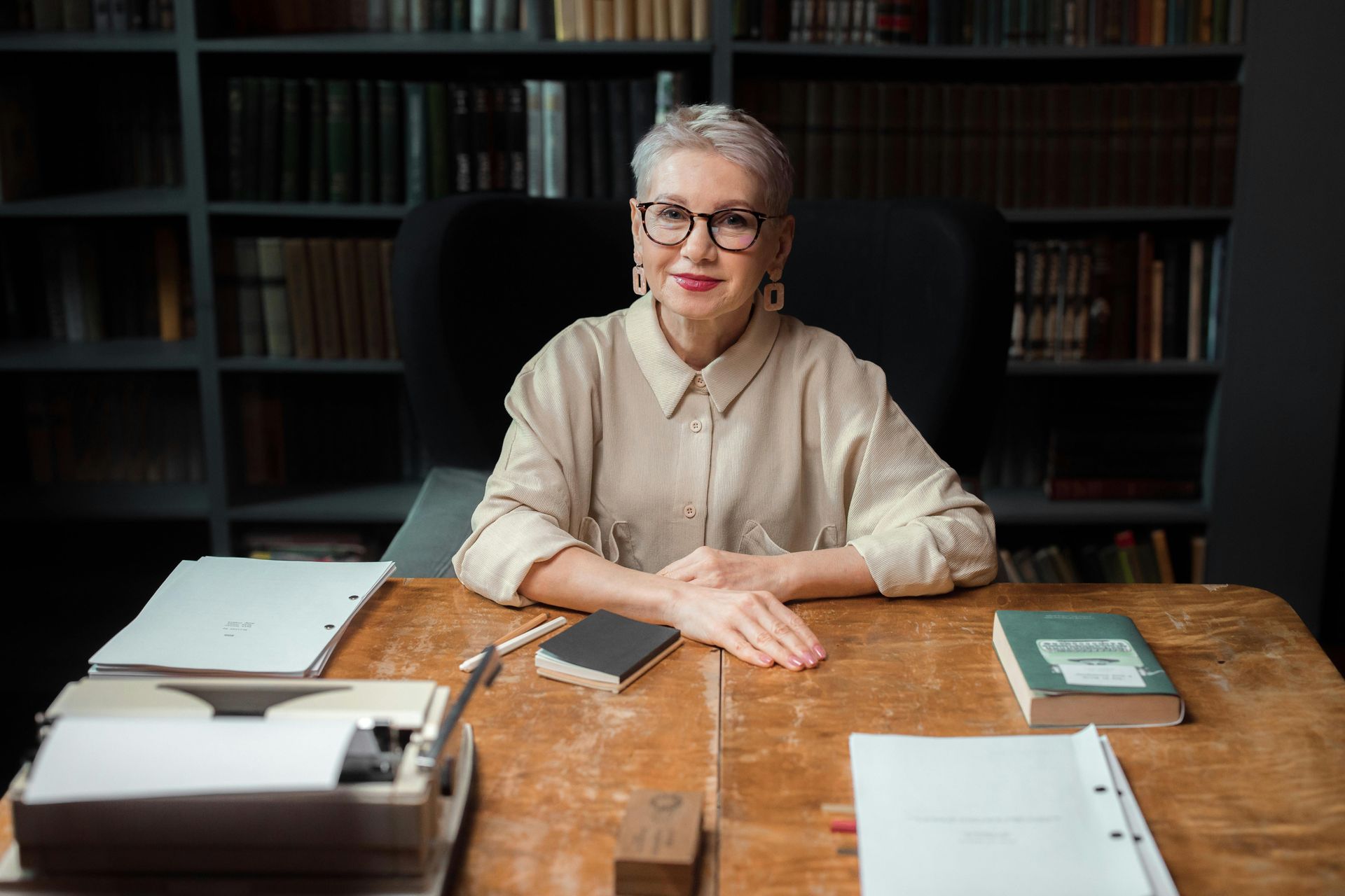 An elderly woman is sitting at a desk in a library.