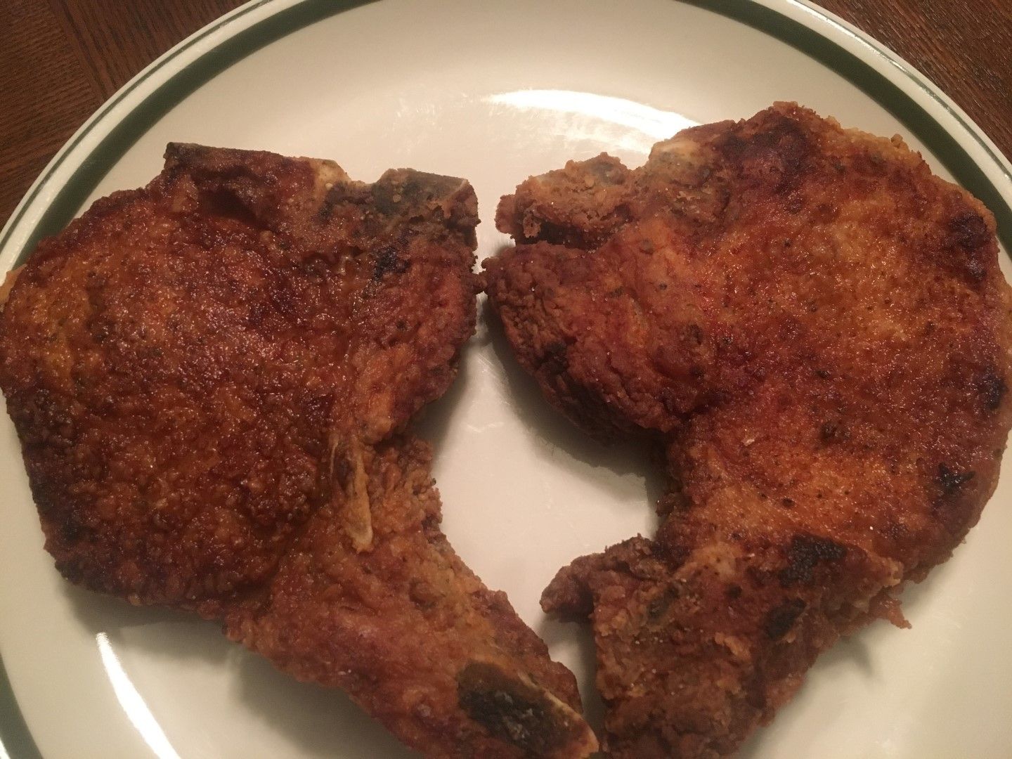 Two fried pork chops on a white plate with a green stripe