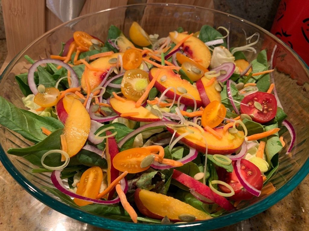 A salad with peaches , tomatoes , carrots , onions and spinach in a glass bowl.
