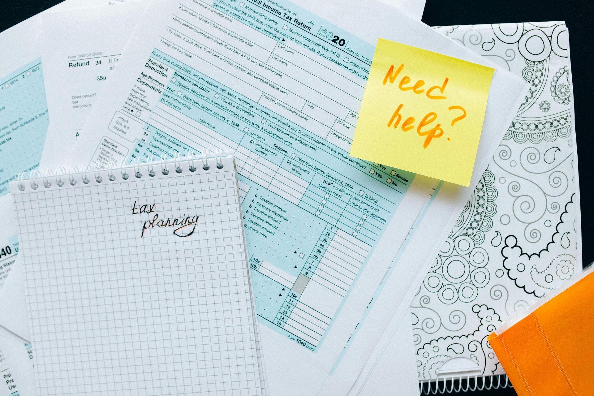 A pile of papers with a yellow sticky note that says need help.