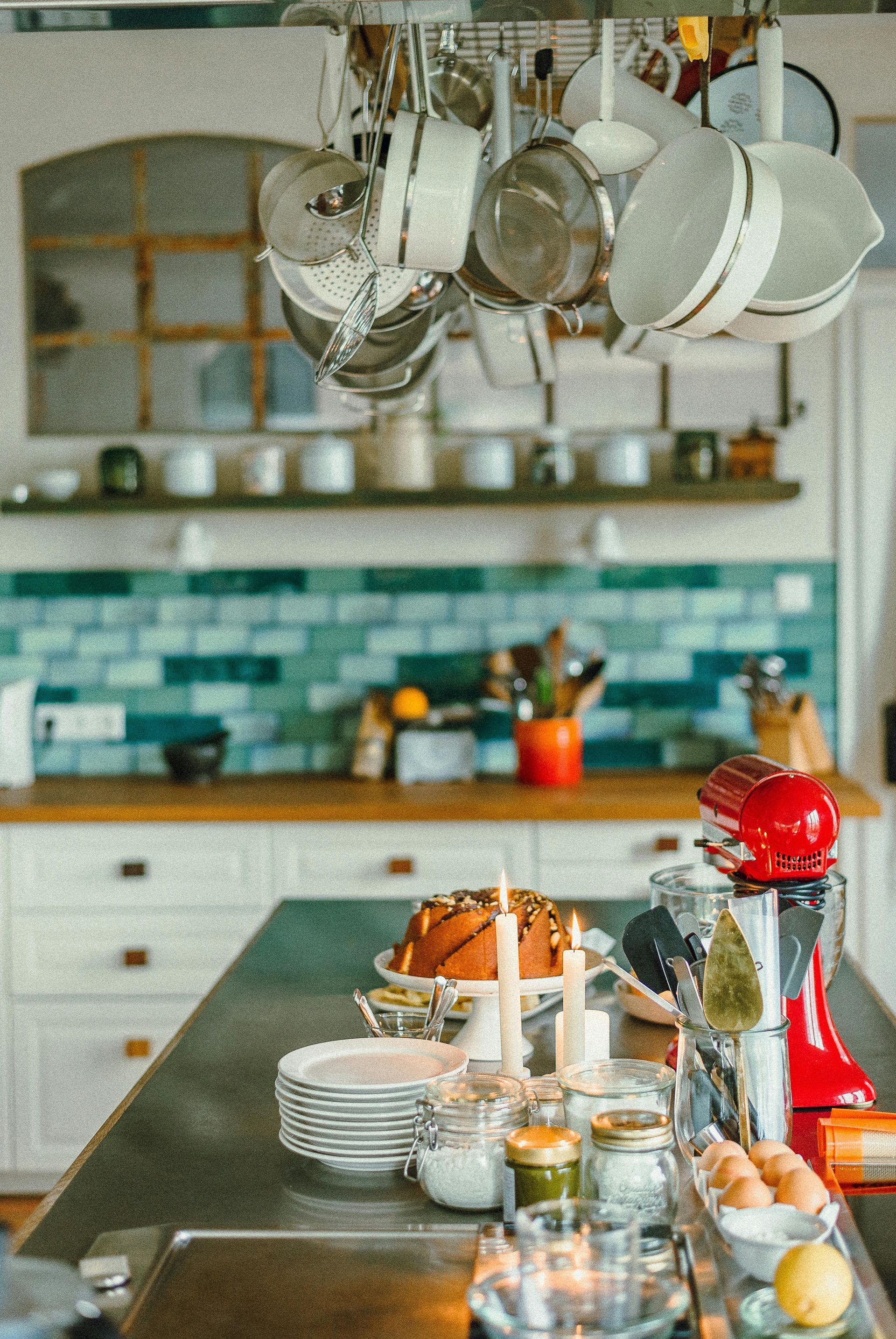 Modern kitchen with hanging pans, turquoise tile backsplash, and a food-prep island with dishes and fruit